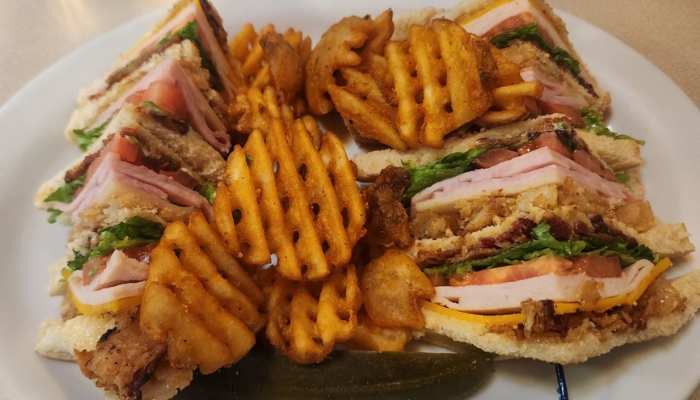 A plate at JC's Country Diner Restaurant Elwood Utah with club sandwiches, waffle fries, and a pickle.