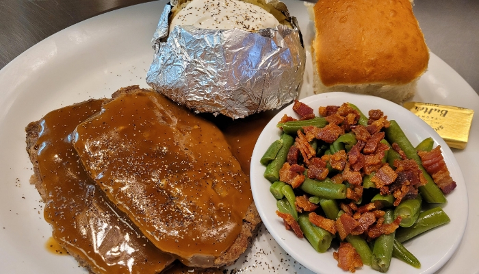 Two slices of meatloaf with gravy, baked potato, and more at JC's Country Diner Elwood Utah.
