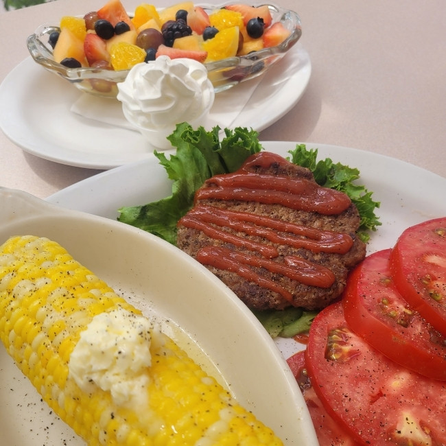 A plate at JC's Country Diner Restaurant Elwood Utah: burger patty, corn, tomatoes, fruit salad.
